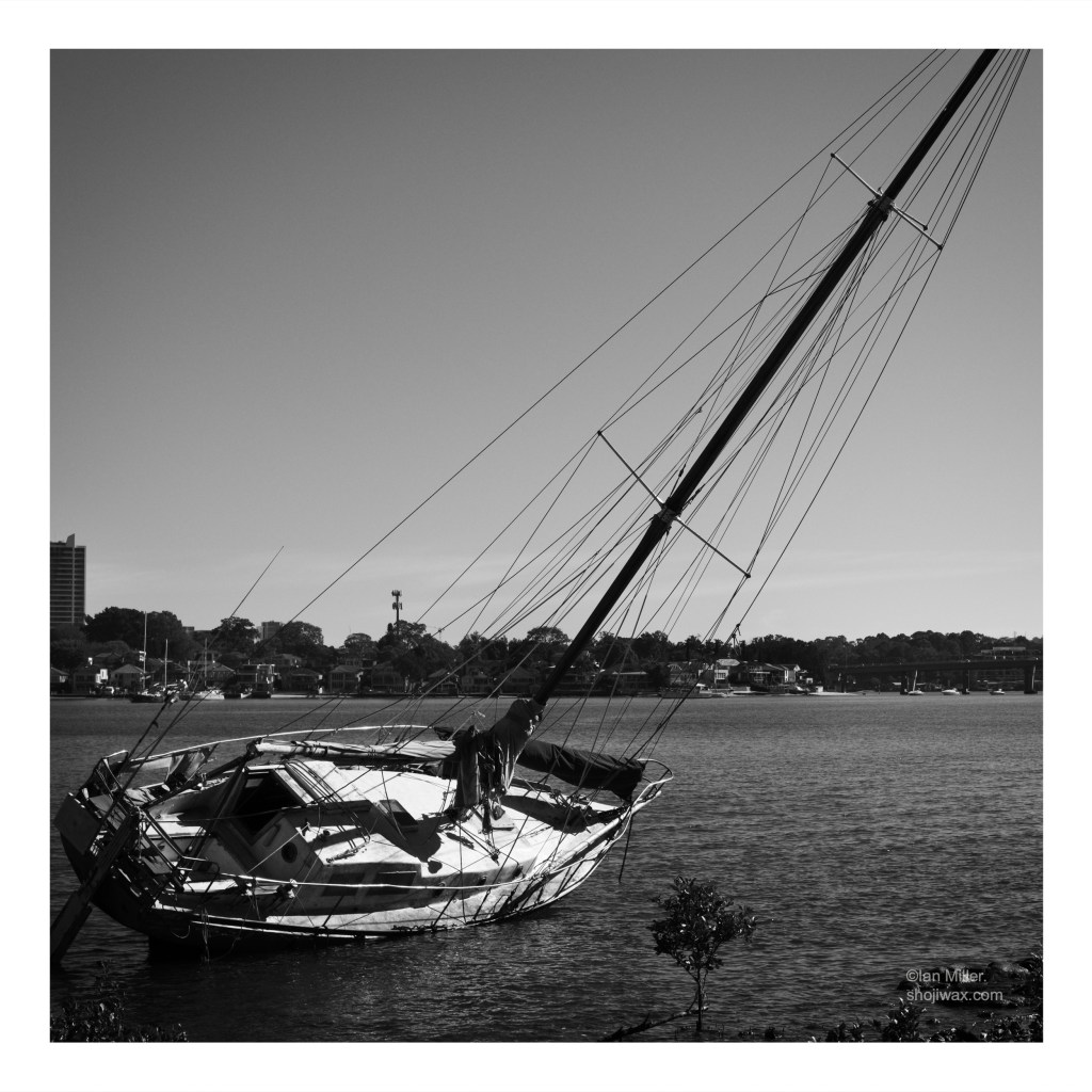 High contrast black and white photo of a small sailing boat that has run aground.