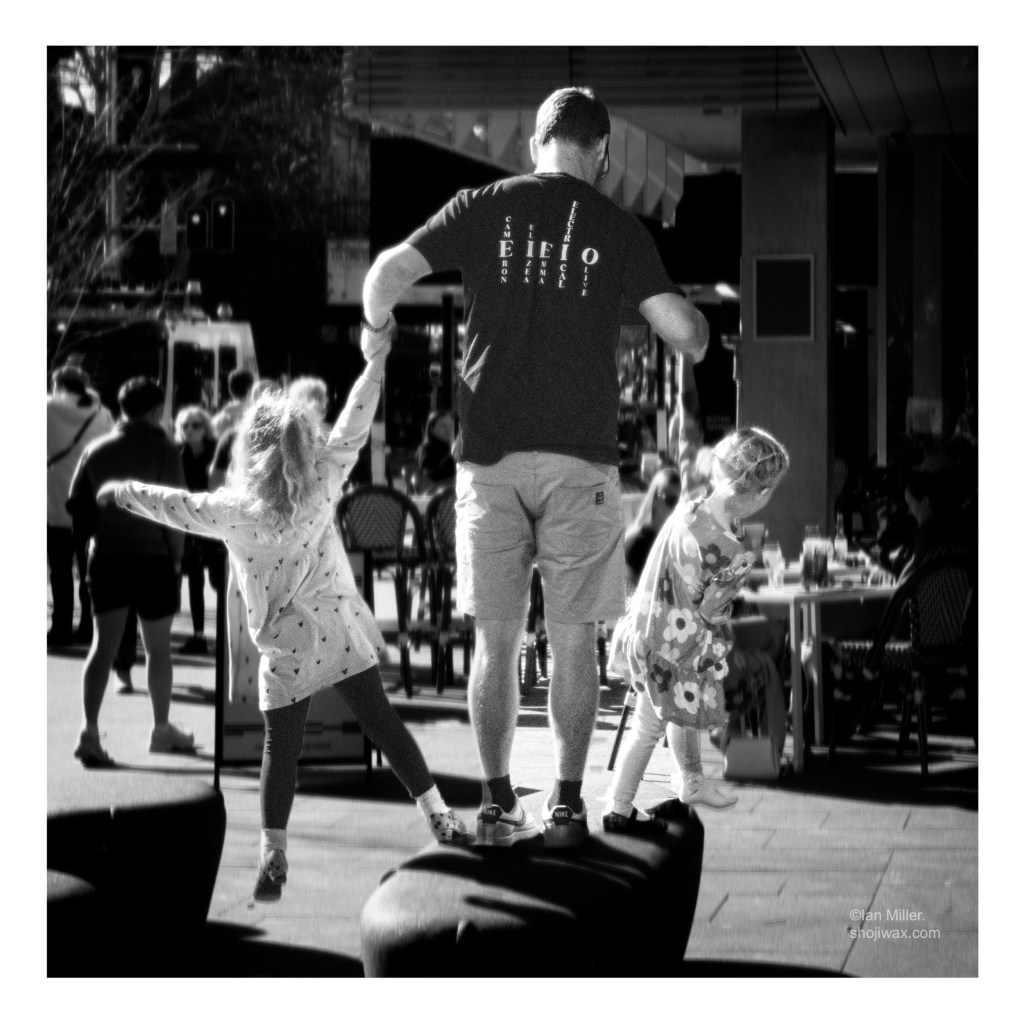 Black and white photo of man holding hands of two young girls who are leaning out in opposite directions