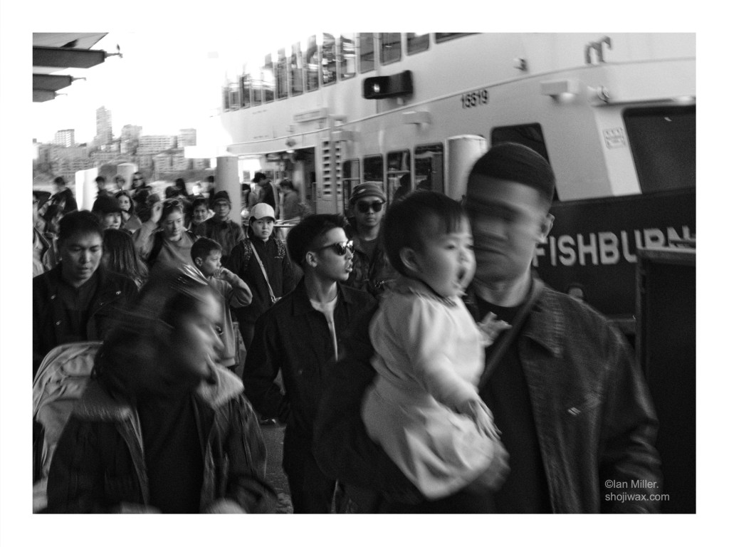 Black and white photo of a crowd of people getting off a ferry. The photo has a slow shutter speed giving a feeling of blurred motion.