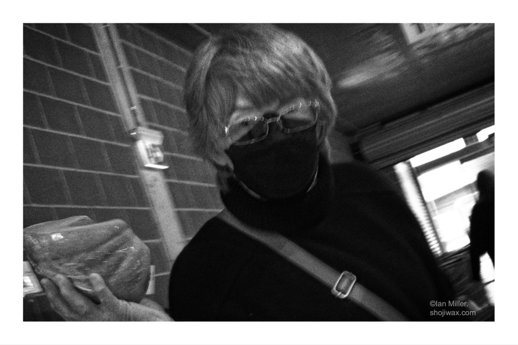Dark and grungy black and white photo of lady waring a mask and holding up a pumpkin wrapped in plastic