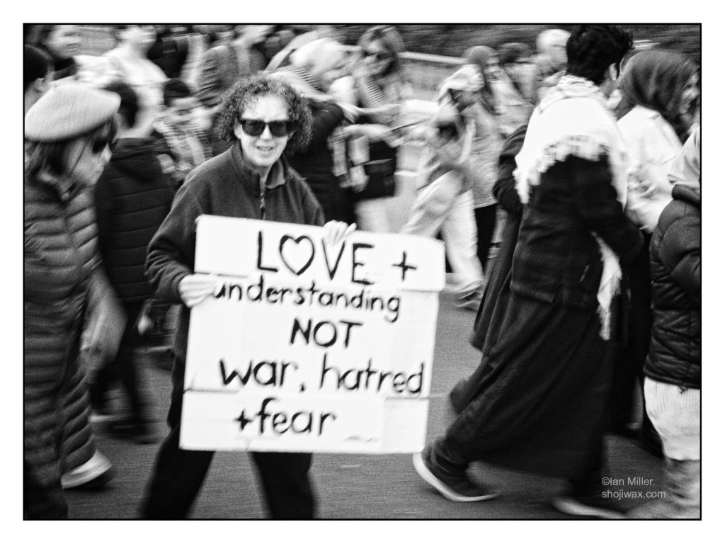 Black and white photo of female protest marcher holding a sign saying: Love and understanding not war hatred and fear.