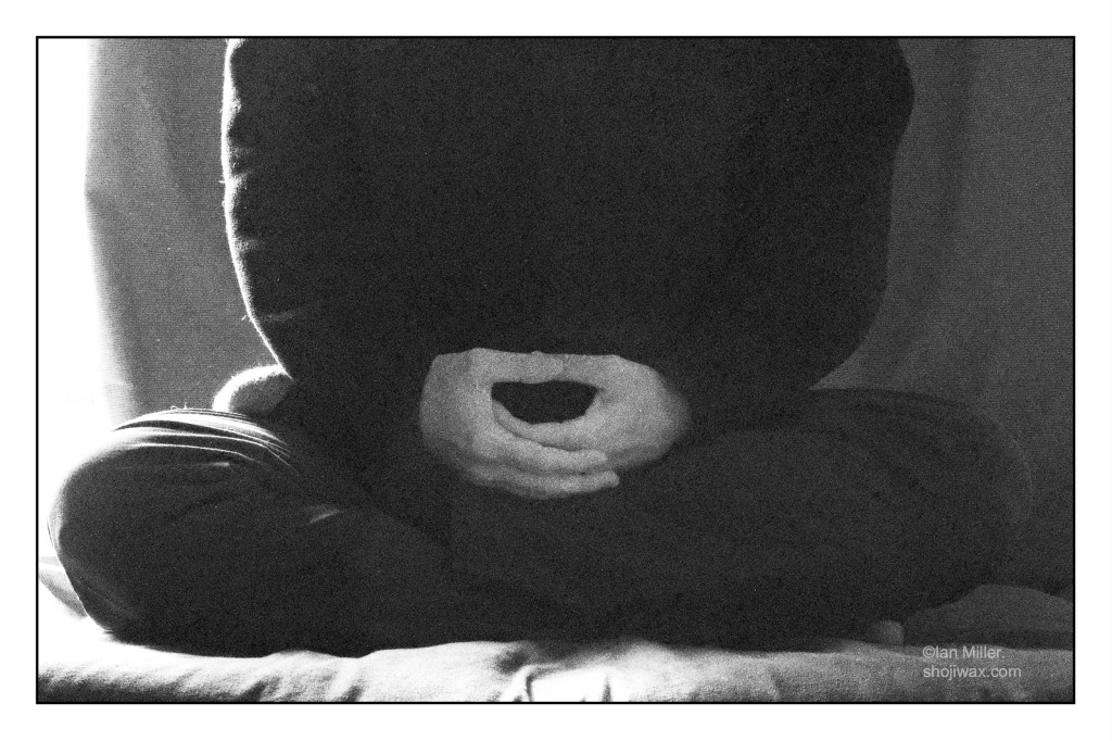 Black and white grainy photo of the lower half of a person sitting in meditation.