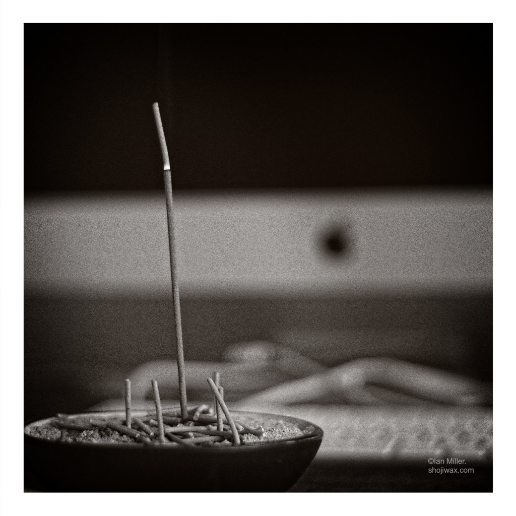 Black and white photo of incense stick burning. In the background are a keyboard and computer screen.