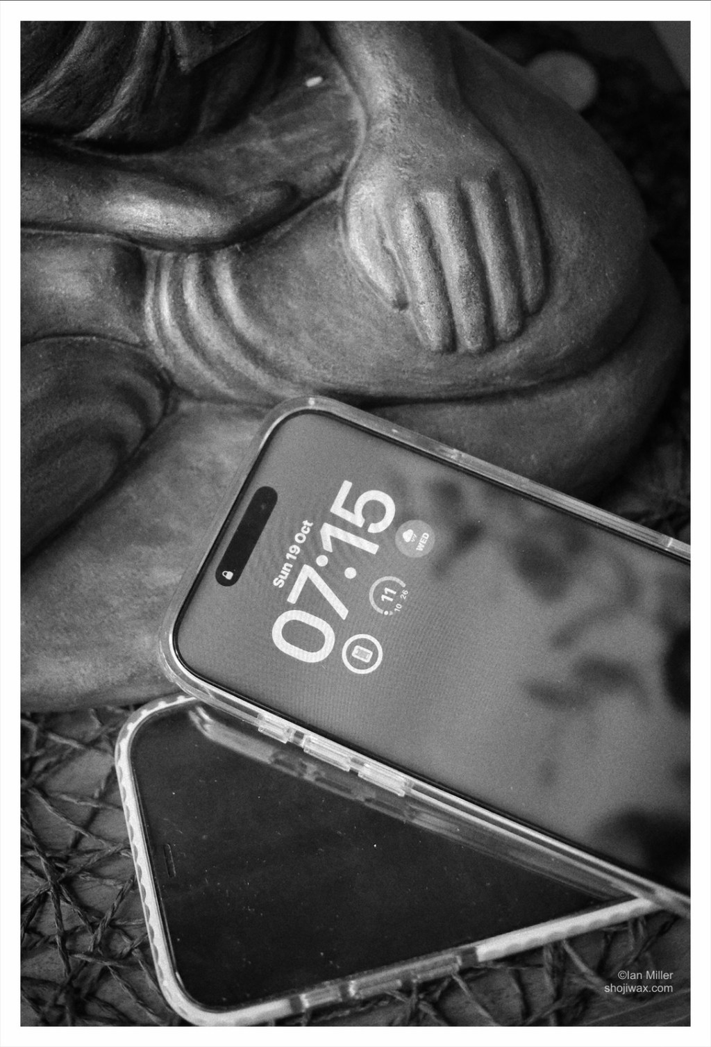 Black and white photo of two iPhones sitting besides the lower half of a buddha statue.