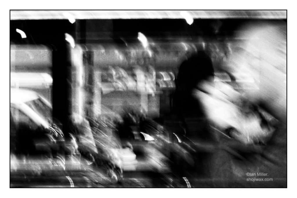 Black and white photo of a man on the right side sitting drinking coffee. The whole photo is motion blurred and out of focus.