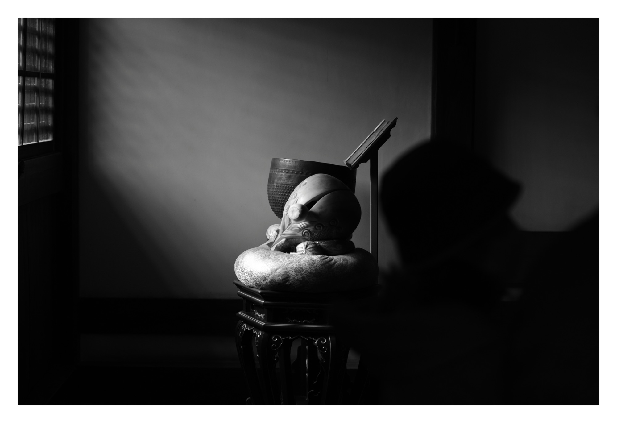 Black and white photo of two Buddhist instruments sitting on a chair. They are illuminated by light streaming in through a wooden window.