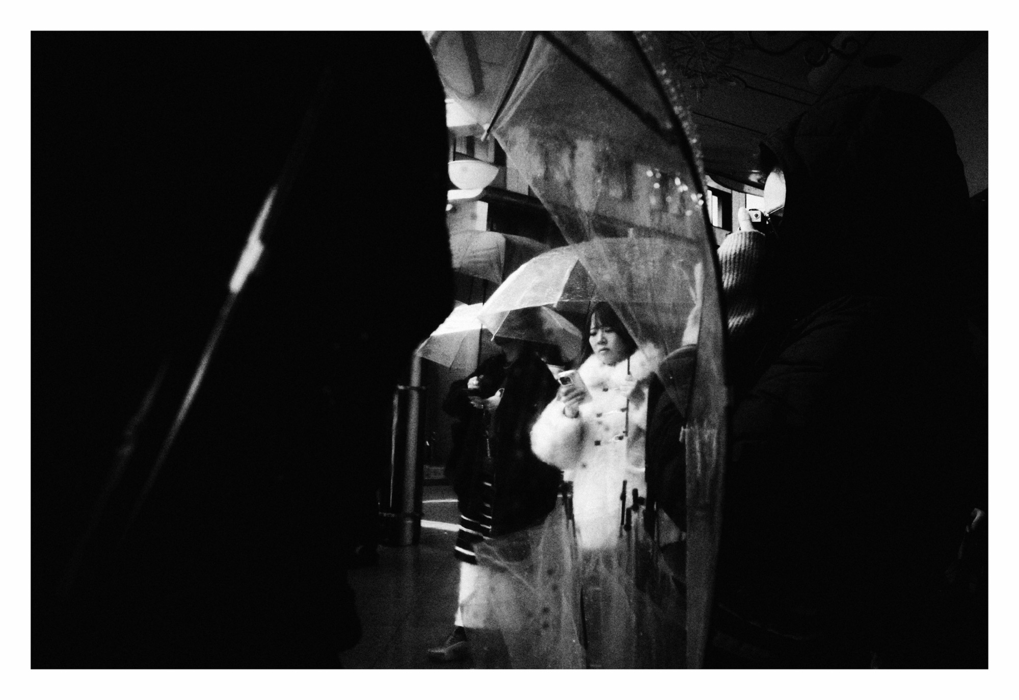 Black and white photo of lady checking her iPhone taken through an umbrella on a rainy day.