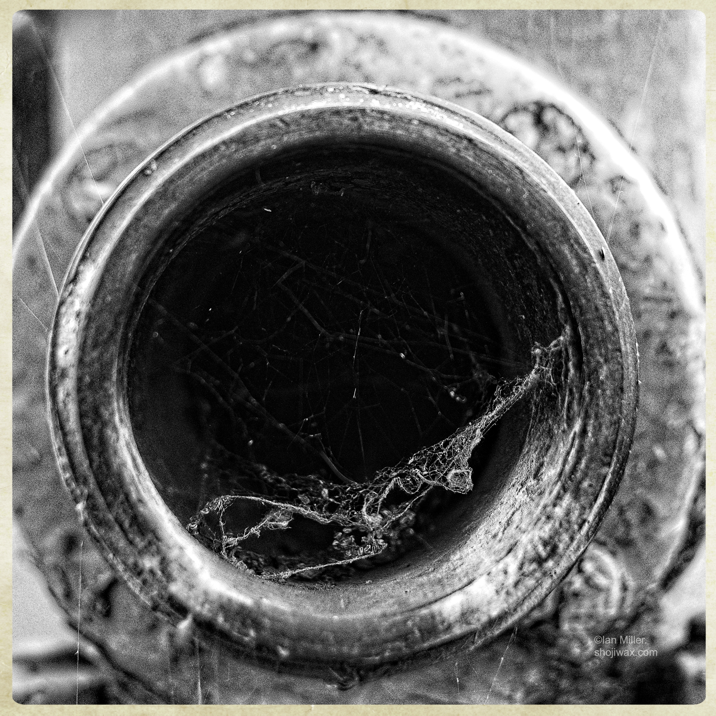 Black and white photo closeup of fire hydrant connector. There is a partial spider web visible across the opening.