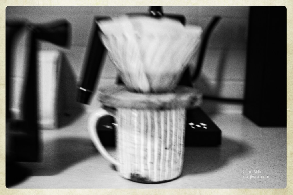 Monochrome, high contrast, out of focus photo of a coffee cup with a filter paper holder on top.