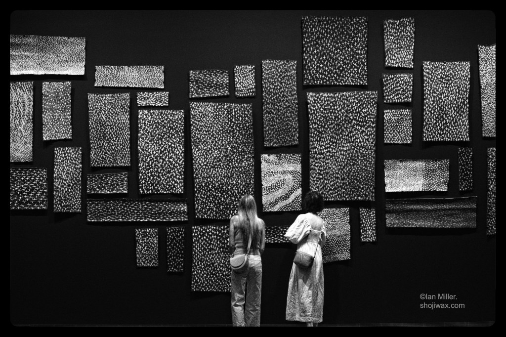 Monochrome photo of two women standing in front of australian first nations paintings of stars.