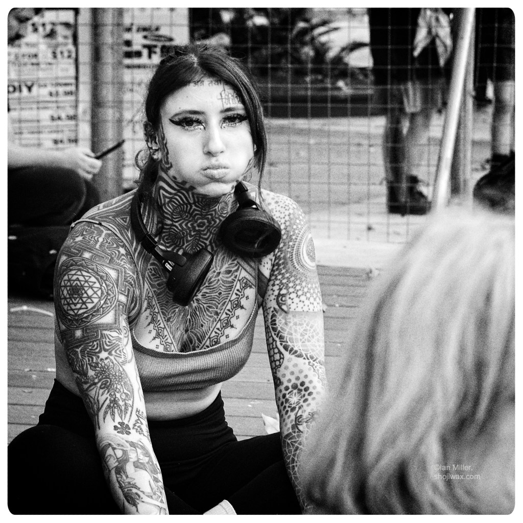 Monochrome photo of woman with extensive tattoos and wearing a set of headphones around her neck.
