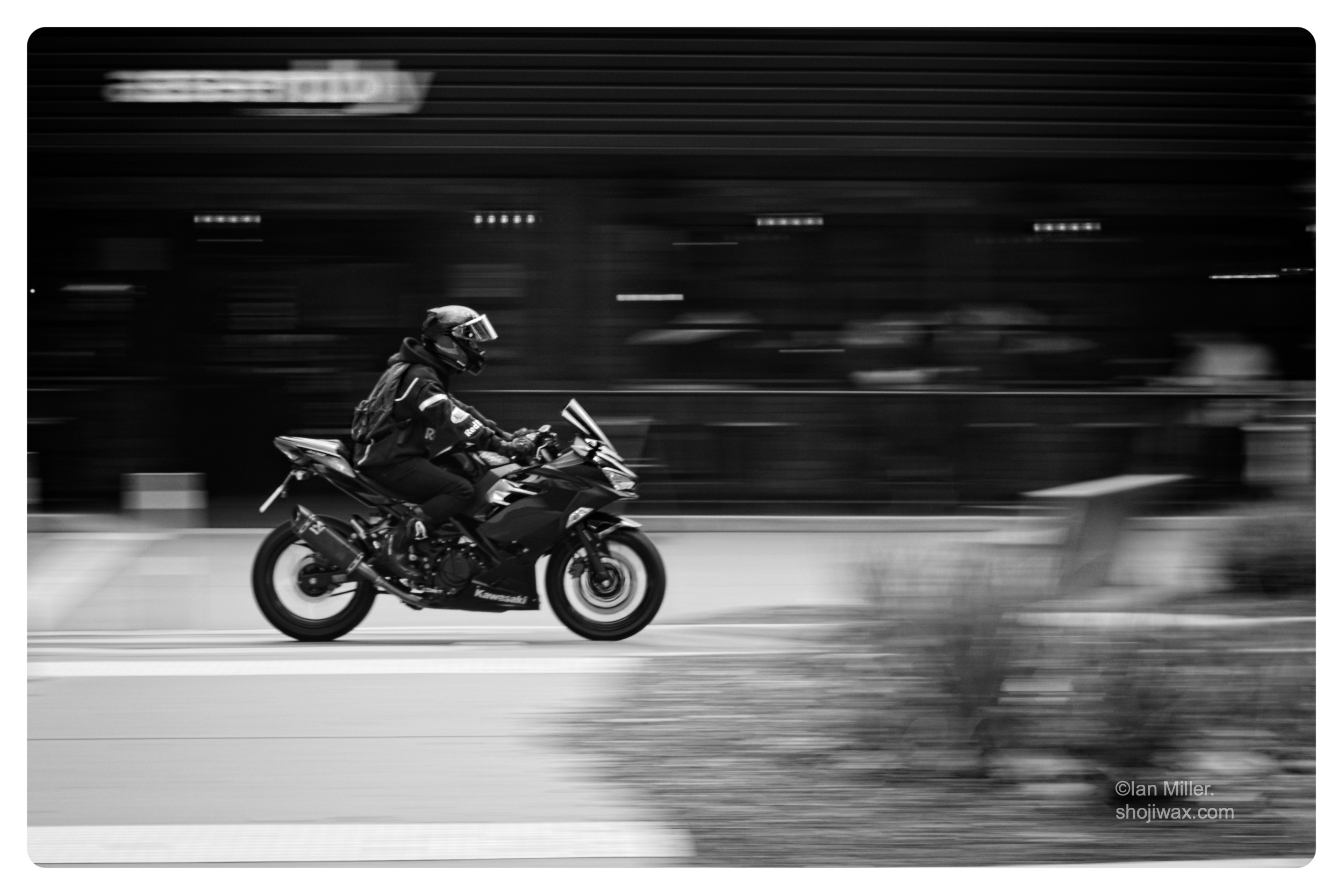 Monochrome photo of motorcyclist riding through a blurred background.