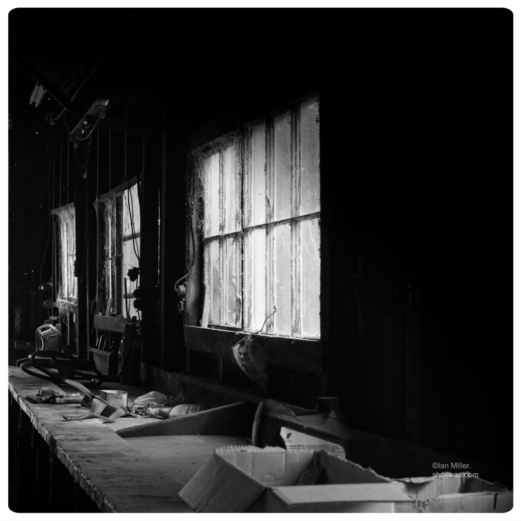 Monochrome photo of dark workbench illuminated by a row of old windows across one wall.