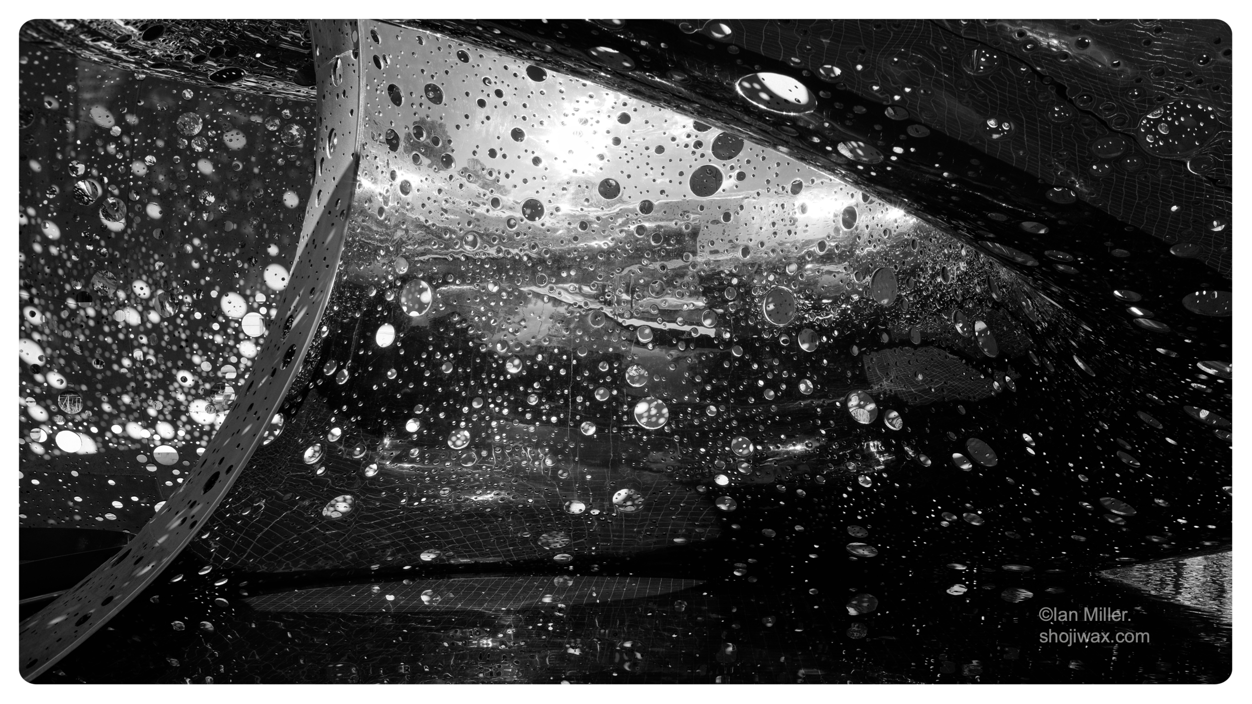 Monochrome closeup of stainless steel sculpture with multiple holes of different sizes letting the light through.