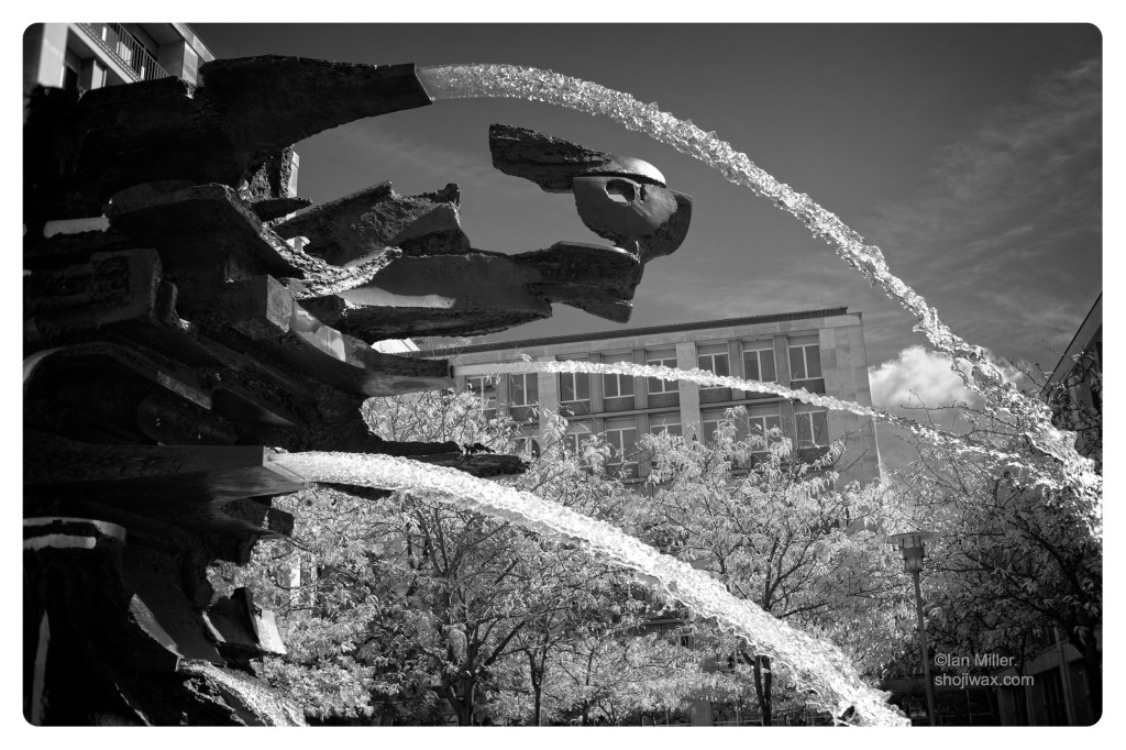 Monochrome photo of large fountain sculpture with multiple water jets.