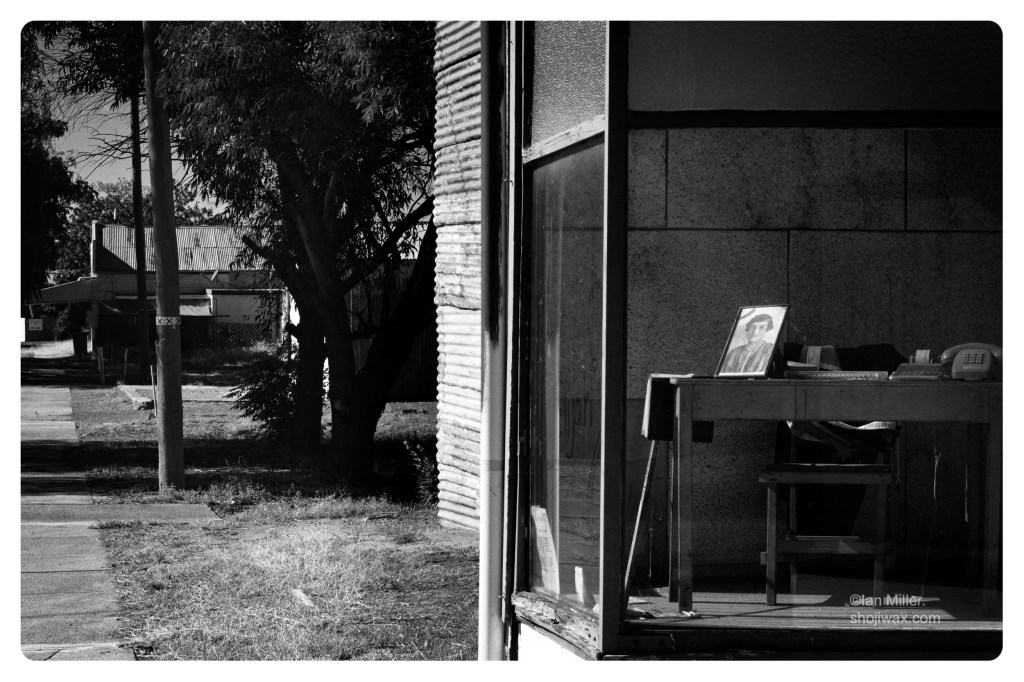 Monochrome photo of a country street with a store window featuring a framed picture of a mysterious woman.