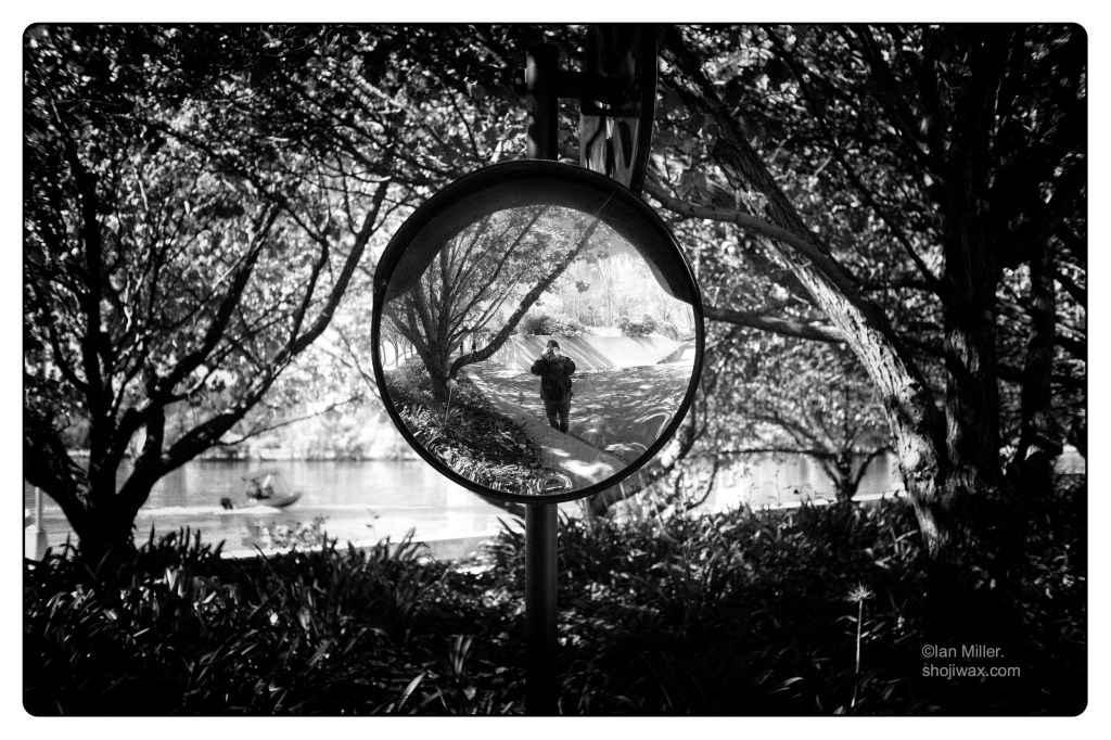 Monochrome photo of me reflected in a convex mirror. in the background are trees and a lake with a speedboat.