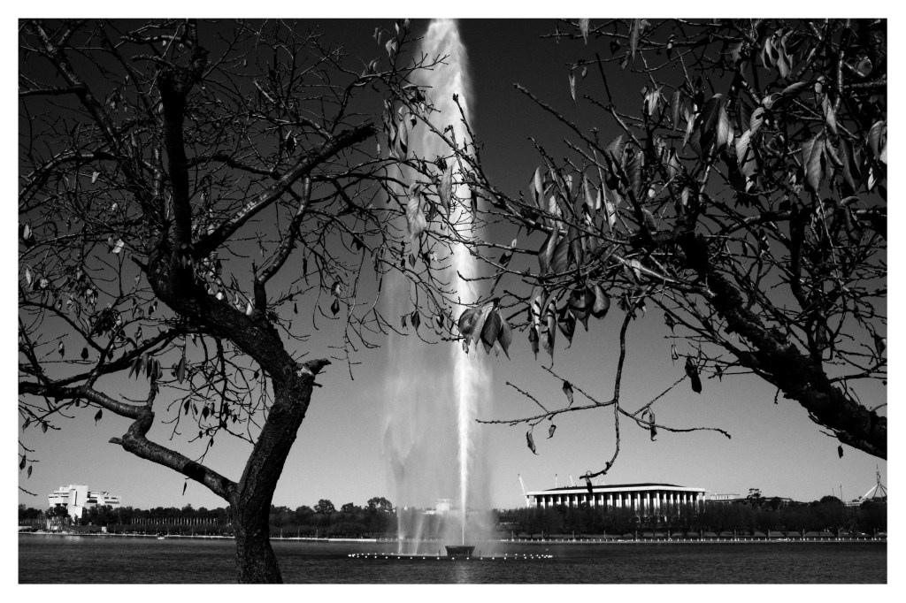 Monochrome photo of large water jet arising from the centre of a lake.