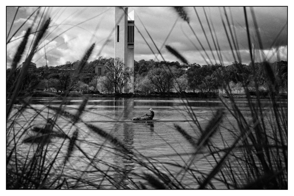 Monochrome photo of a man rowing in front of a Carilion