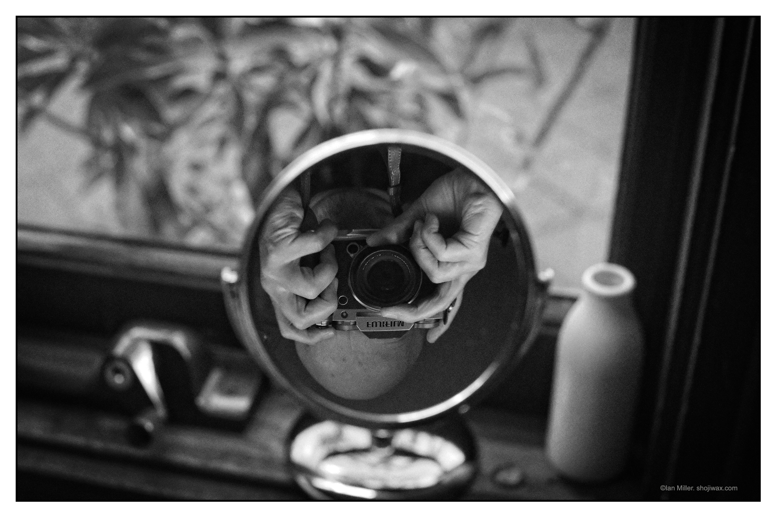 Monochrome photo of a selfie of the photographer inverted and reflected in a circular mirror on a windowsill