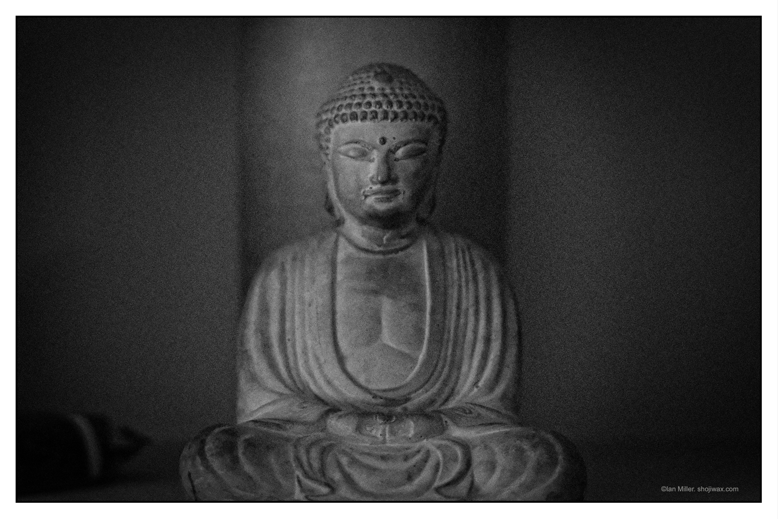 Monochrome photo of a small plaster Buddha seated in meditation.