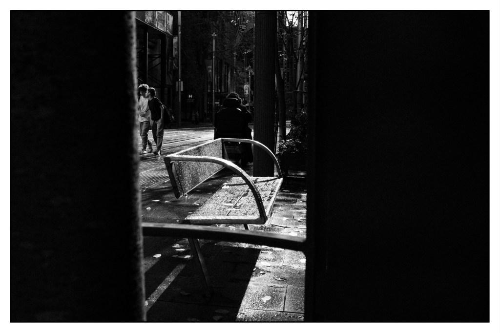 Monochrome photo of city park-bench covered in raindrops.