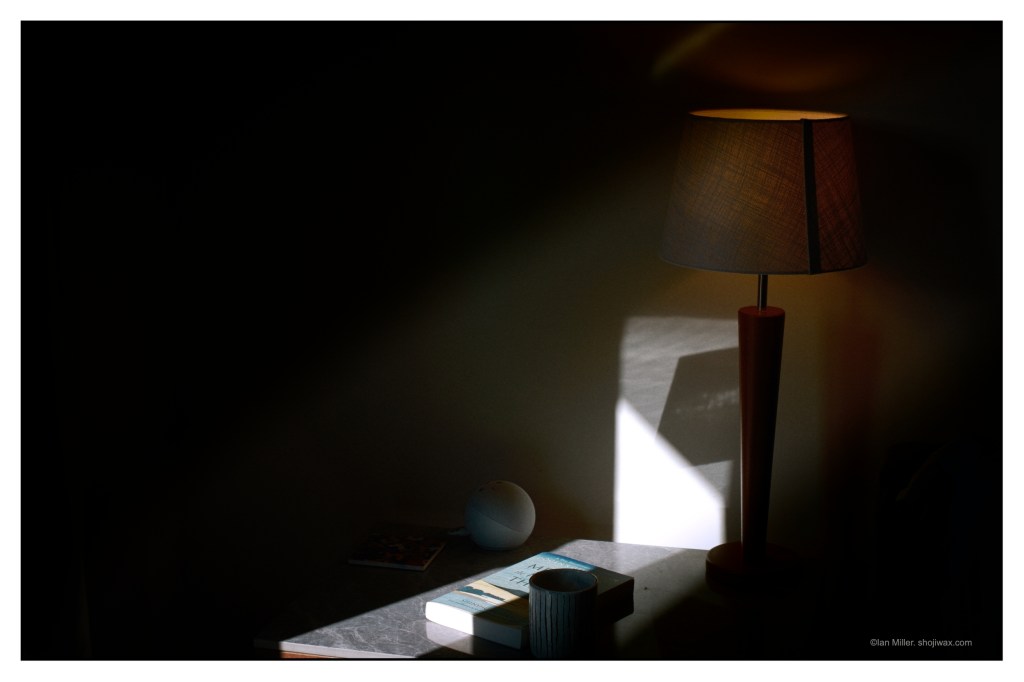 Photo of a table lamp casting an orange glow whilst itself lit by a shaft of sunlight.