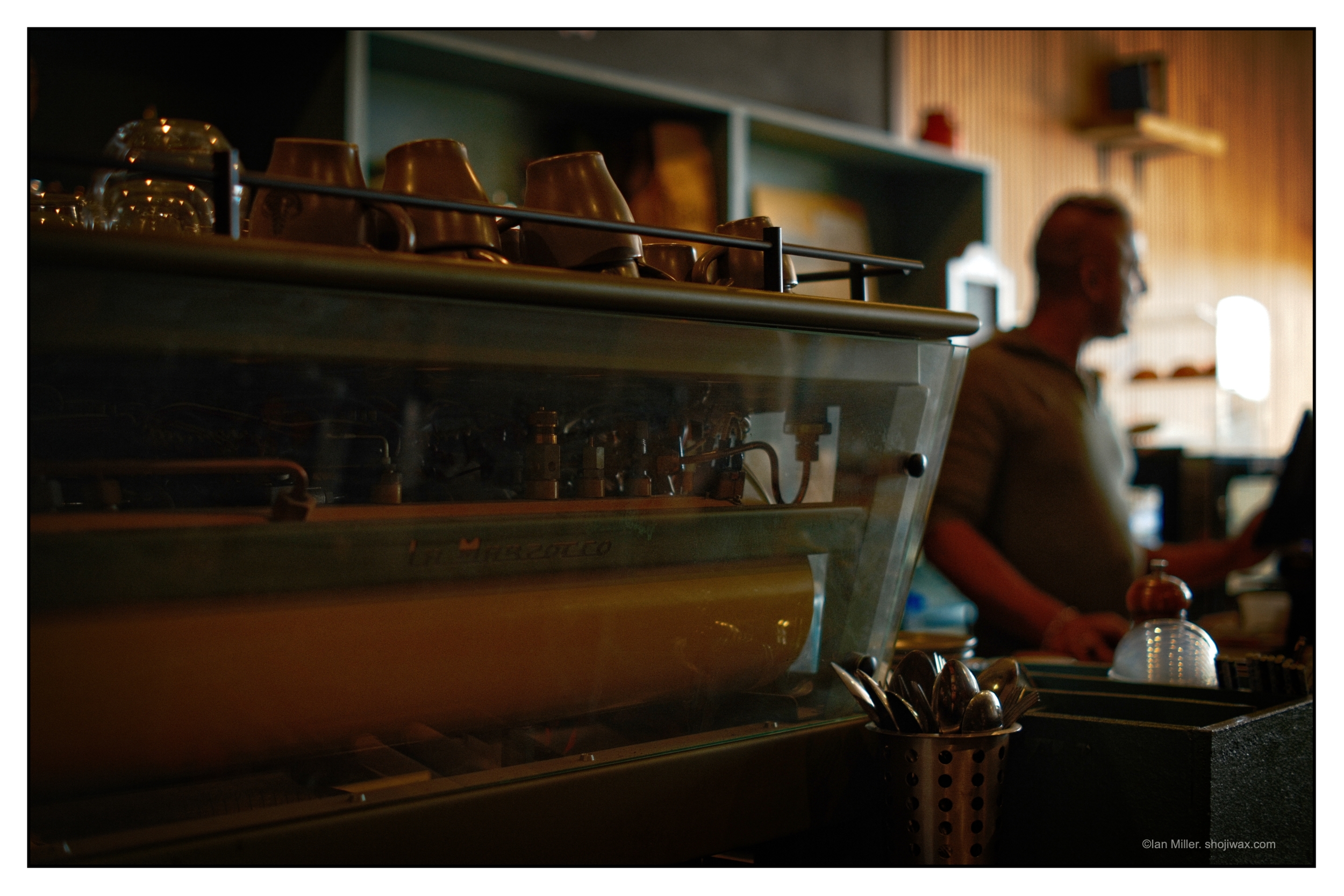 Colour photo of retro cafe espresso machine with barista in the background.