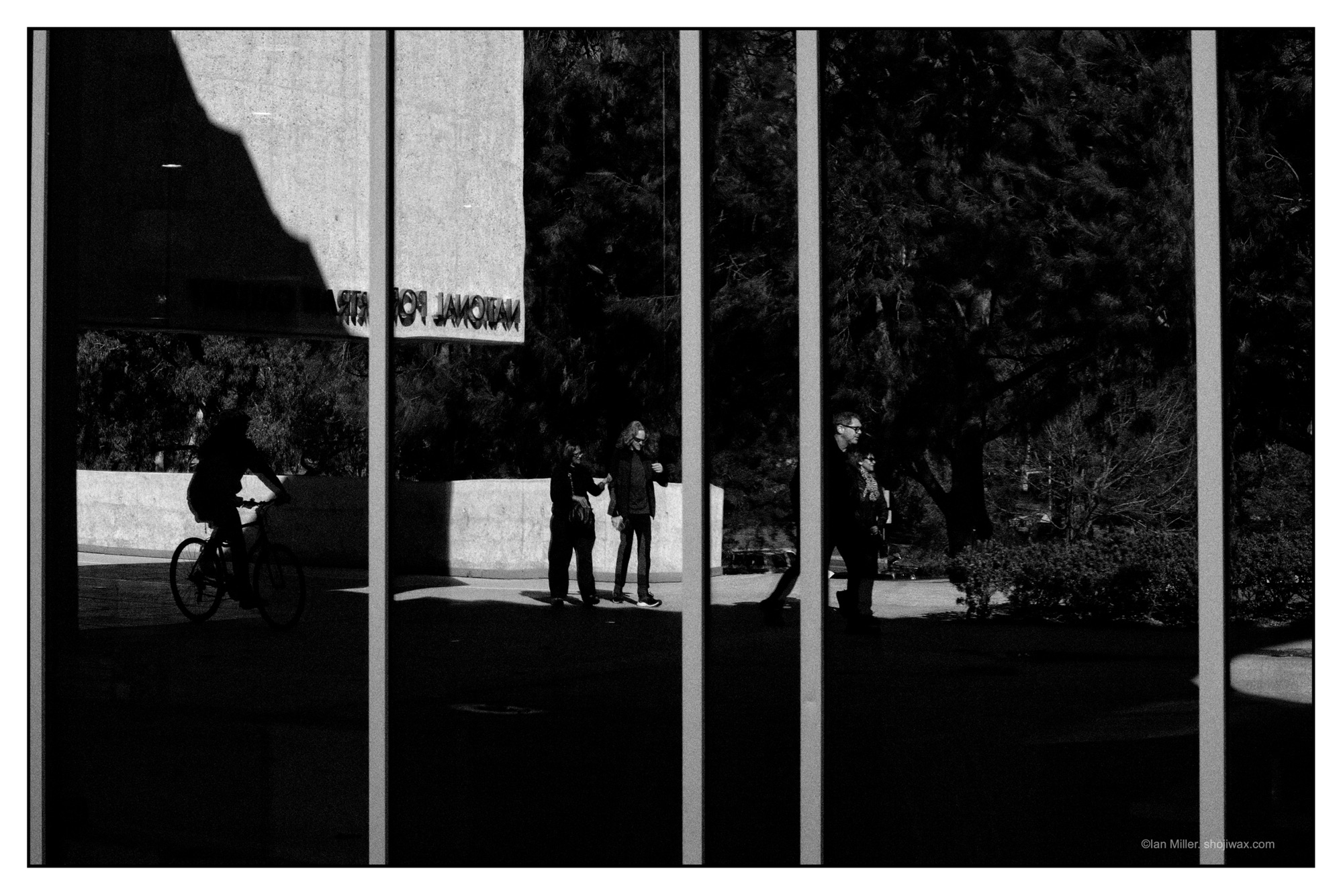 Dark monochrome photo of a group of people walking reflected in a framed window.