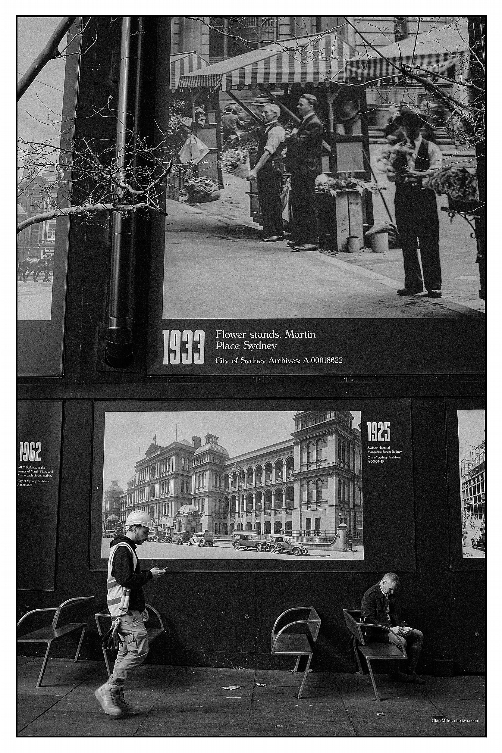 Monochrome photo of two men in front of a billboard depicting photos of sydney from 1933