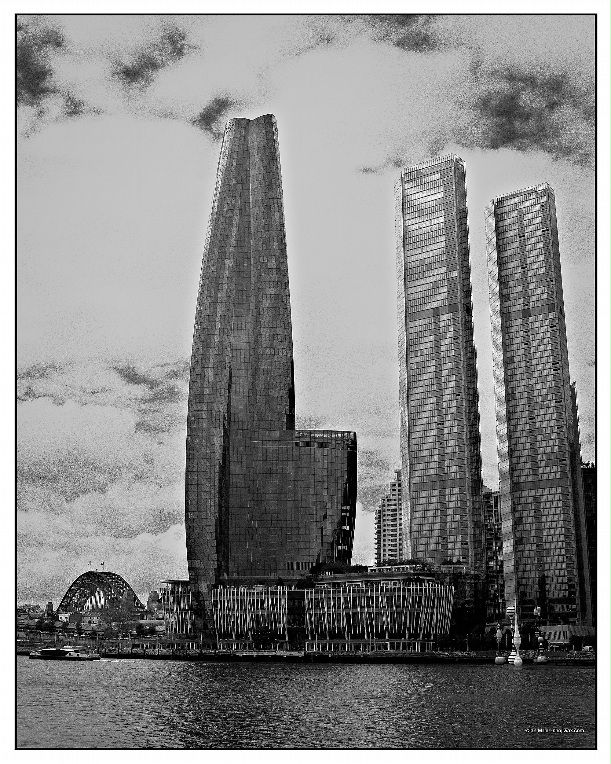 Monochrome photo of 3 tall modern buildings taken from across the harbour. In the background can be seen the Sydney Harbour Bridge.