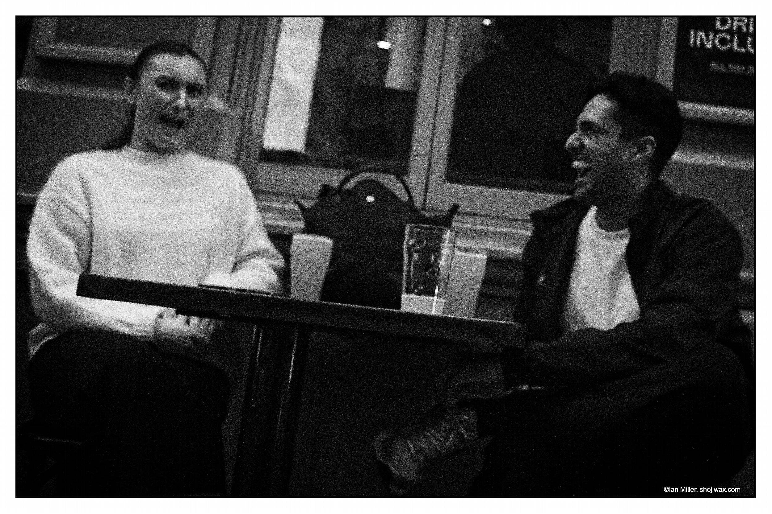 Monochrome photo of two people seated at an outdoor table at night....laughing hard.