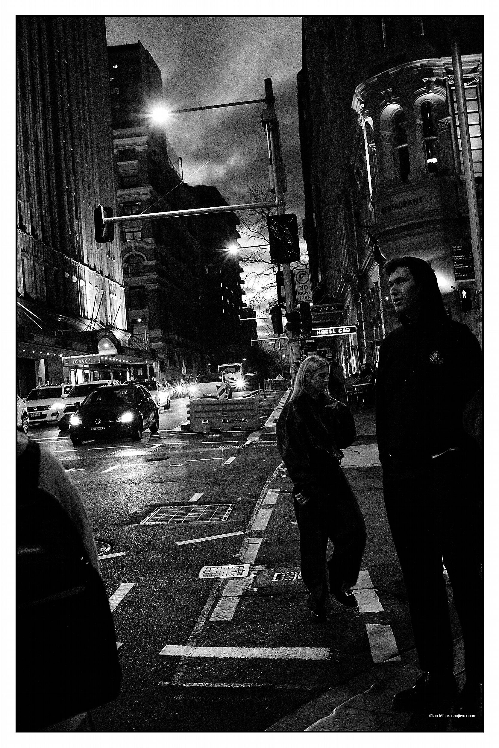 Monochrome photo of a man and a woman standing at a busy intersection at night.