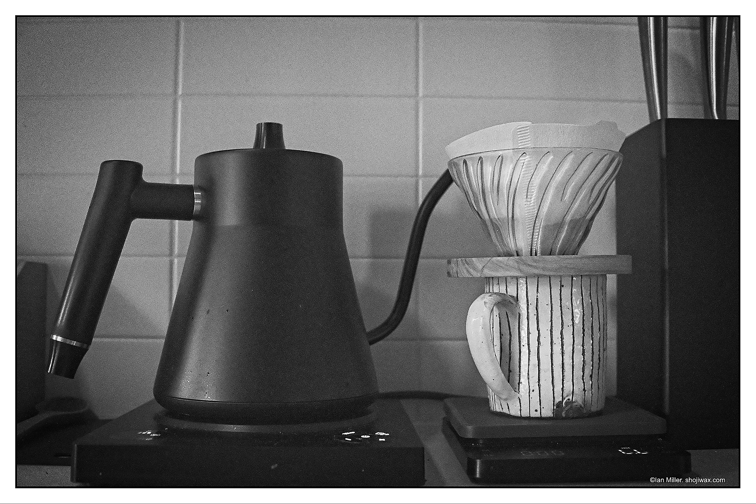 Monochrome photo of a swan-neck kettle and a cup with a V90 pourover atop it.